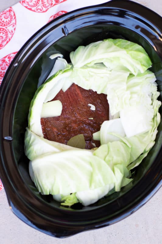 Crockpot filled with a brisket topped with raw cabbage. 