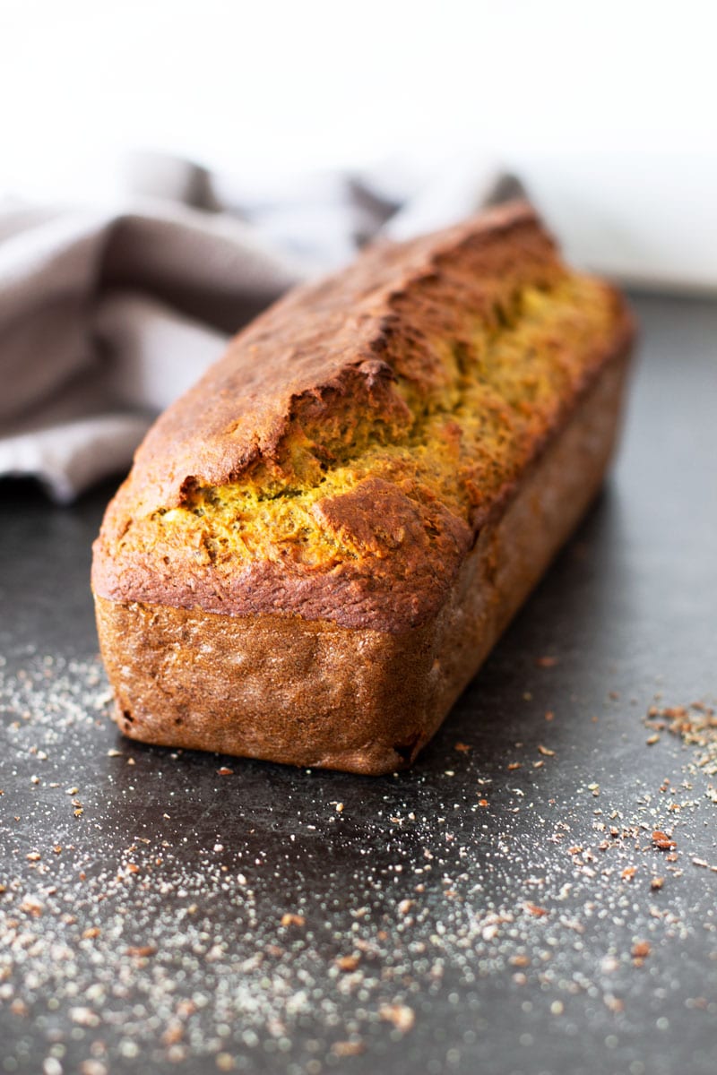 Loaf of quinoa banana bread on a marble table, nuts sprinkled on table.