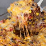 Spatula containing a piece of mexican casserole topped with melted cheese.