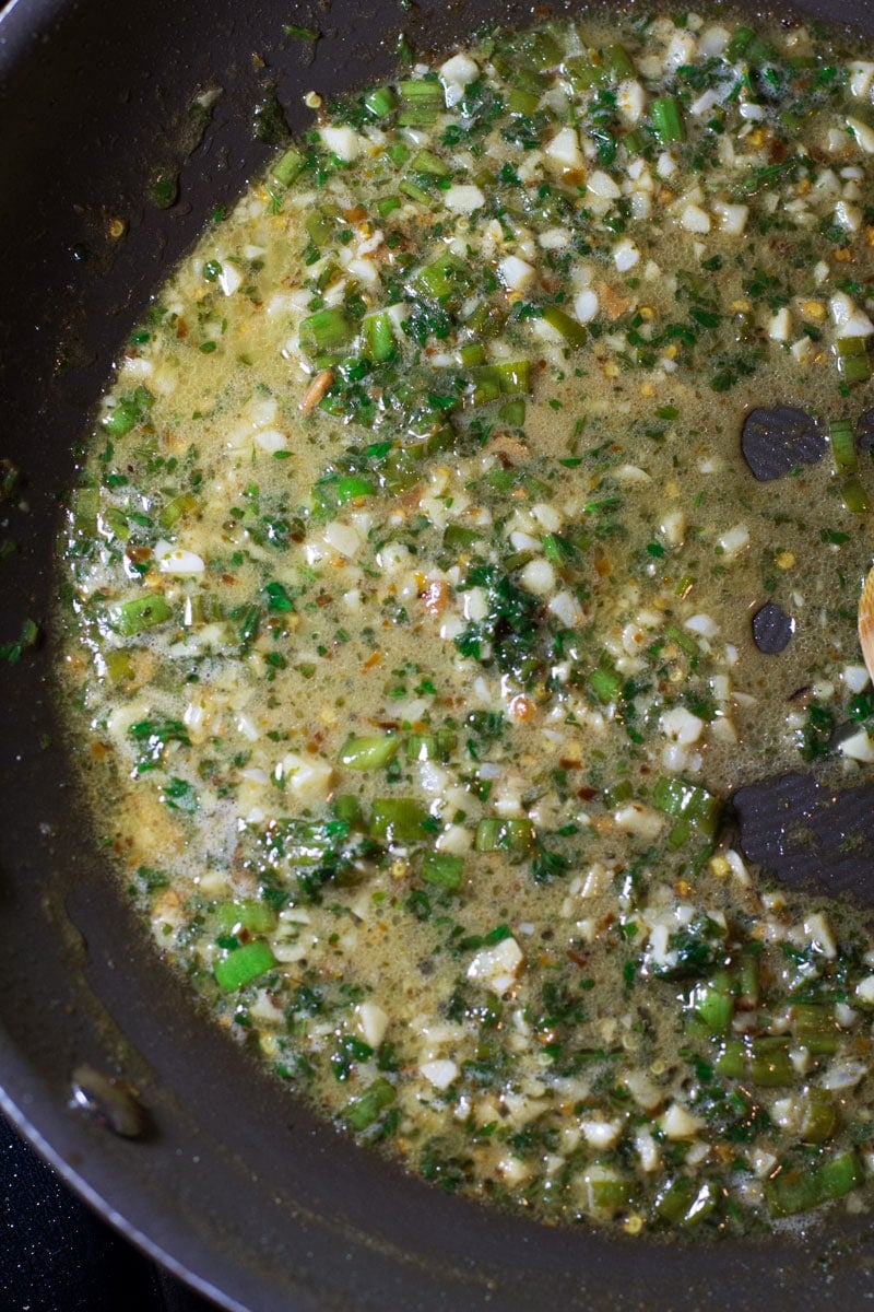 Skillet containing sauce made with garlic, parsley, lime, scallions, and butter.