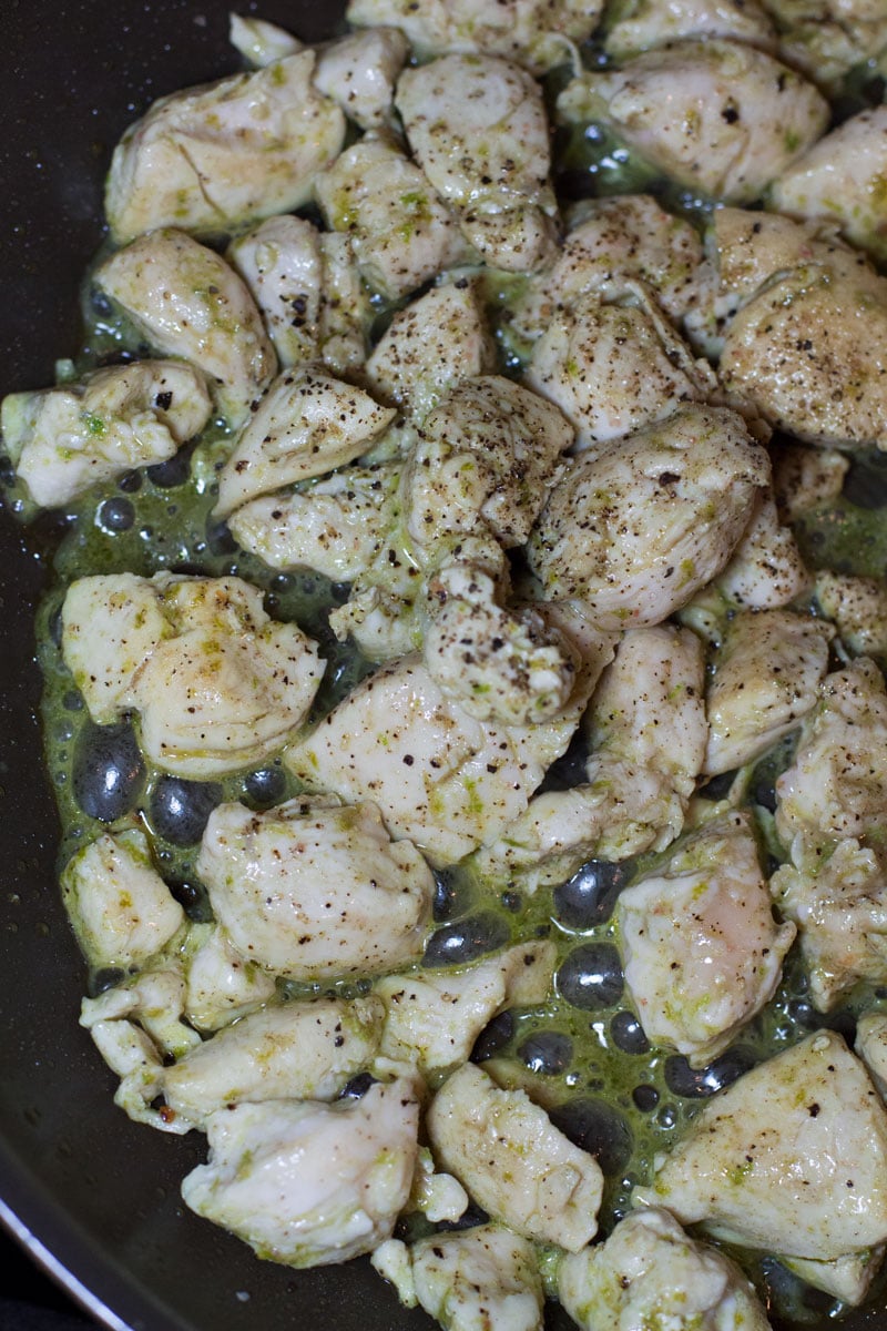 Chicken sauteing in a skillet with herbs and olive oil.