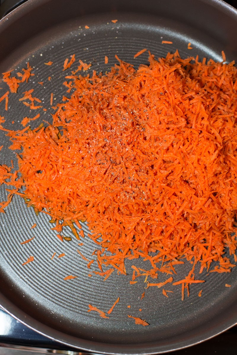 Skillet containing grated carrots with salt and pepper.