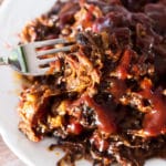 Fork containing shredded ribs topped with BBQ sauce on a white plate.