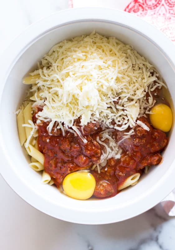 White bowl containing pasta, marinara sauce, mozzarella cheese, and eggs.