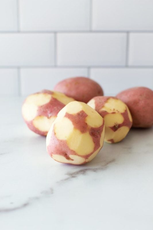 Half peeled red potatoes on a white counter table.