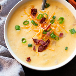 Bowl of Loaded Baked Potato Cheese Soup with bacon, green onion, and cheese on table.