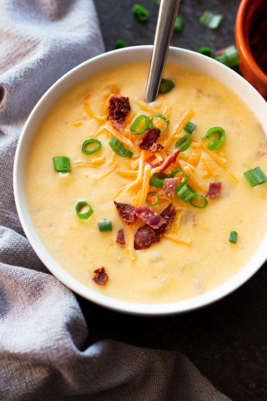 White bowl containing loaded potato cheese soup topped with green onions, bacon, and cheese.
