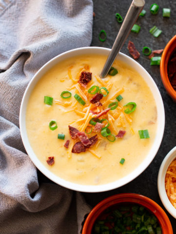 Bowl of Potato Cheese Soup, spoon in bowl topped with cheese, bacon, and onions.