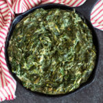 Cast iron skillet containing backed creamed spinach recipe on counter.