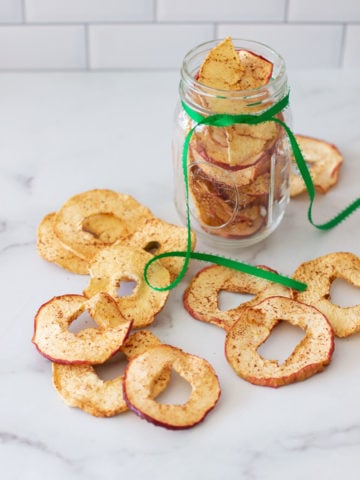 Jar filled with dehydrated cinnamon apples, apple rings on table.