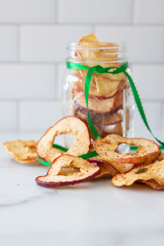 Dehydrated Apple Cinnamon apples on a marble counter and in a mason jar.