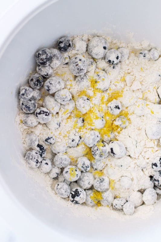 White bowl containing blueberries and fresh lemon zest covered in flour.