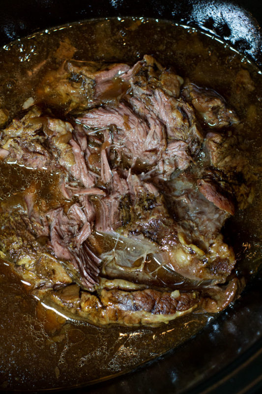 Shredded beef in a crockpot filled with juices and seasonings.