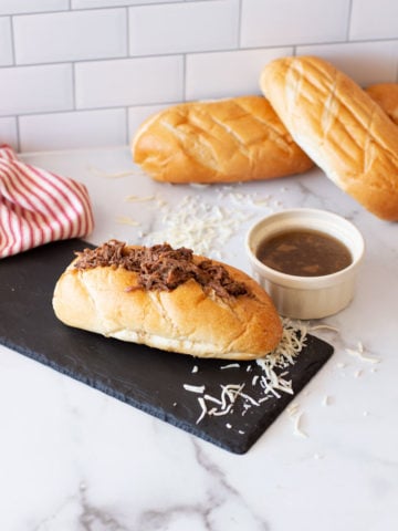 French Dip Sandwich on a counter, au jus dipping sauce and bread on counter.