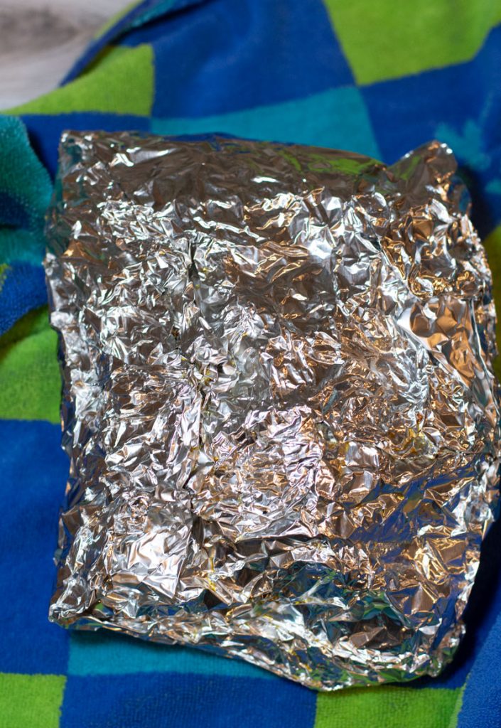 Double aluminum foil smoked pork butt being wrapped in a beach towel.