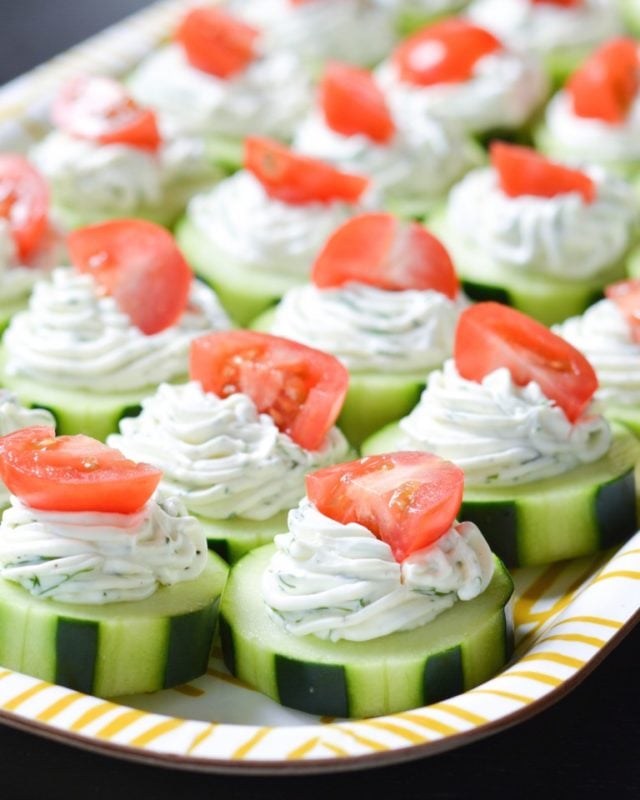 Sliced cucumbers with piped cheese and yogurt topped with tomatoes.