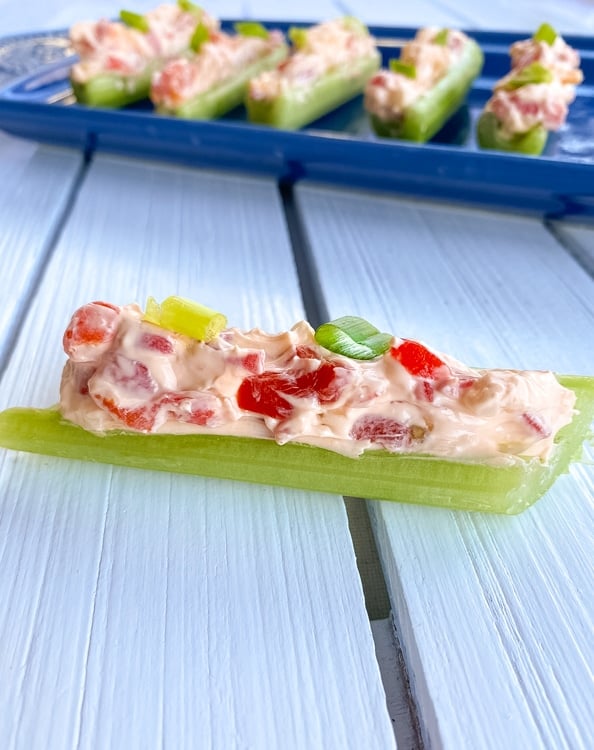 Stick of celery filled with cream cheese and pimento peppers on a table.