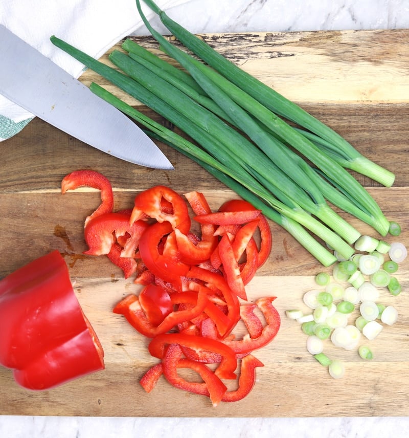 Chopped red pepper and green onion on wooden table.