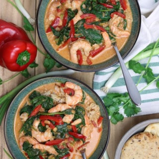 Two green bowls containing shrimp curry topped with spinach and red pepper, onions and peppers on table.