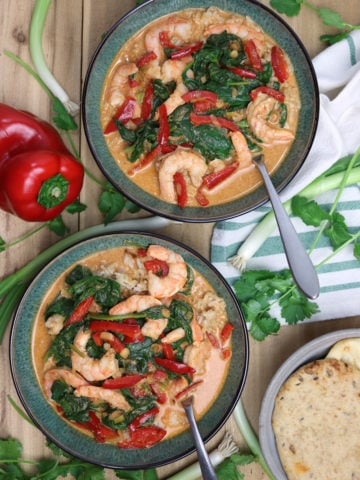 Two green bowls containing shrimp curry topped with spinach and red pepper, onions and peppers on table.
