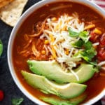 Close up of chicken tortilla soup topped with cheese and avocado.