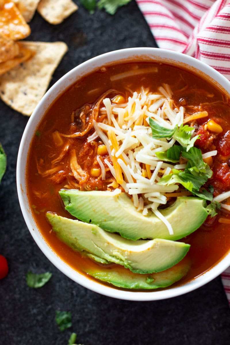 Close up of a bowl of chicken tortilla soup topped with cheese, avocado, and cilantro.