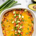 Mexican Chicken Casserole in a white casserole dish topped with avocado, onions, and tomato.