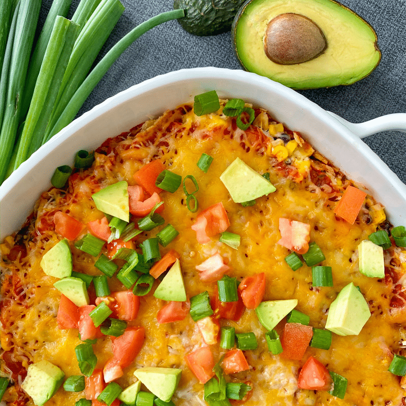 Mexican Chicken Casserole in a white casserole dish topped with avocado, onions, and tomato.