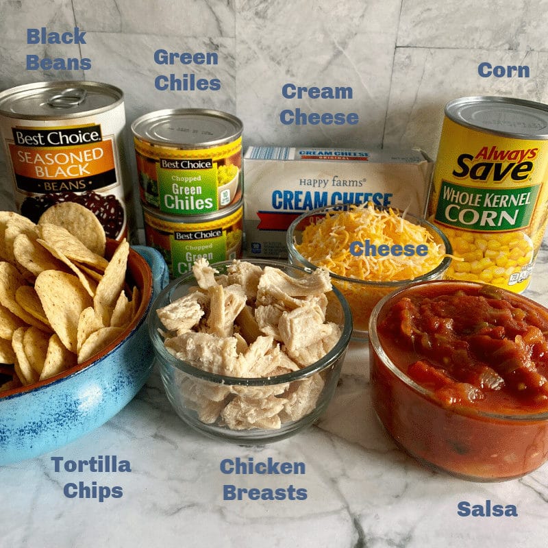 Black beans, tortilla chips, green chiles, corn, cream cheese, chicken, salsa and cheese on counter.