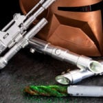 Green lightsaber churro on a table next to a Star Wars helmet and guns.