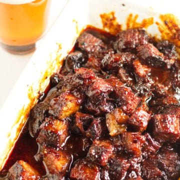 White dish with smoked brisket burnt ends in a kansas city-barbecue sauce with a glass of beer