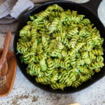 Skillet containing pasta with avocado sauce, Parmesan and pepper on table.