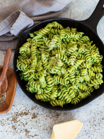 Skillet containing pasta with avocado sauce, Parmesan and pepper on table.