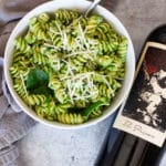 White bowl containing avocado pasta with red wine on table.