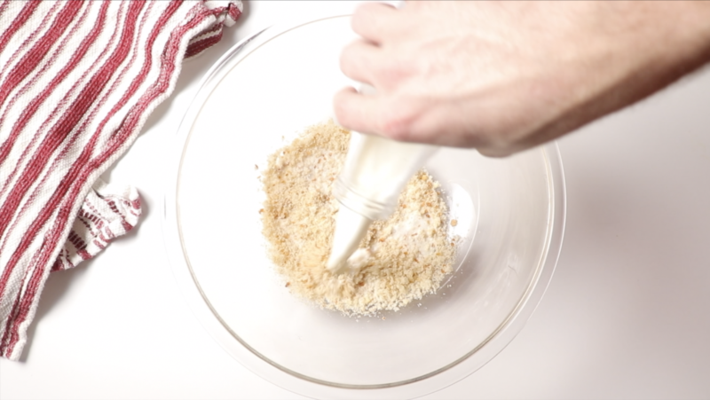 breadcrumbs in a glass mixing bowl with milk being added, red and white towel