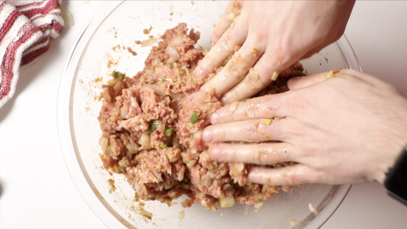meatloaf mixture being mixed by hand in a glass mixing bowl on a white counter