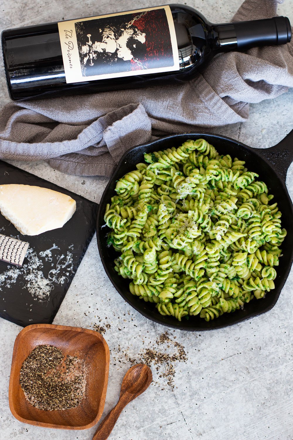 Skillet containing avocado pasta, wine, Parmesan cheese, and pepper on table.