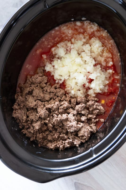 A close up of a slow cooker containing meat and stew ingredients.