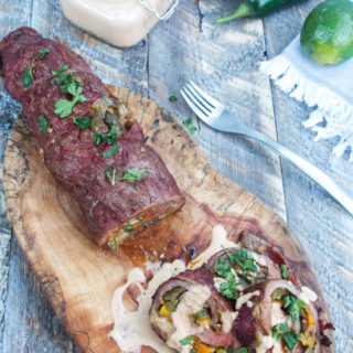 grilled fajita stuffed flank steak with a chipotle lime crema sauce sitting on a wooden background