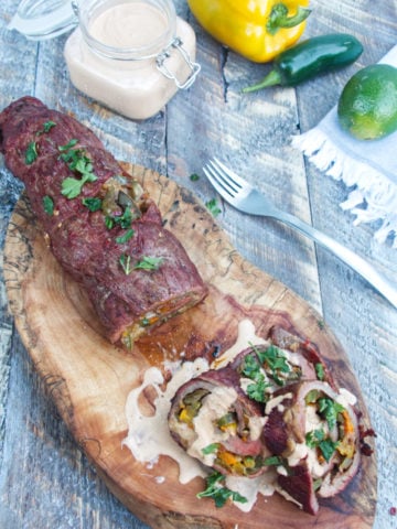 grilled fajita stuffed flank steak with a chipotle lime crema sauce sitting on a wooden background
