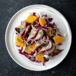 White plate with radicchio salad topped with roast duck and mint.