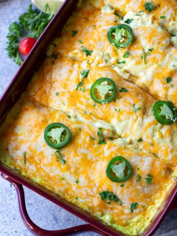 Chicken and cheese enchiladas in a glass dish topped with cilantro and jalapenos.
