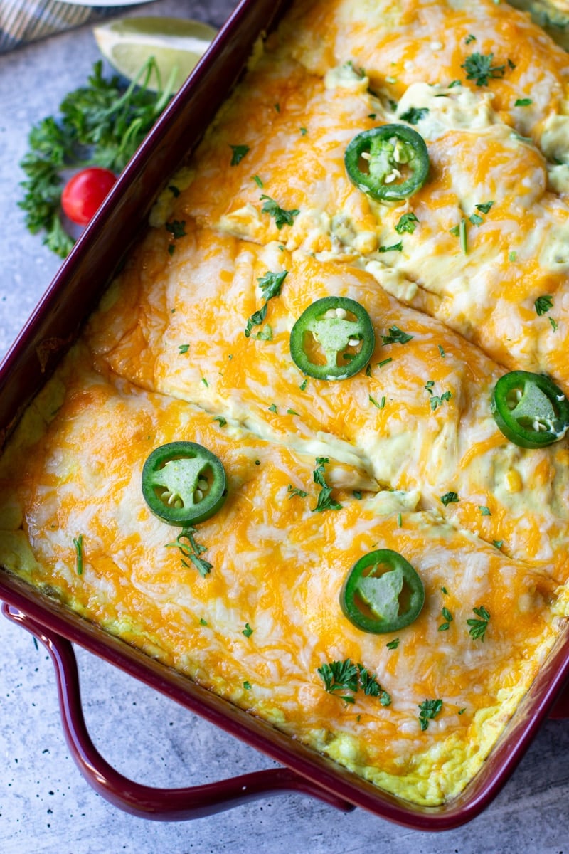 Chicken and cheese enchiladas in a glass dish topped with cilantro and jalapenos. 