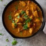 Skillet containing a red chicken curry made in an Instant Pot, topped with fresh cilantro.