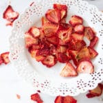 White plate containing strawberry chips, dried strawberries on counter.
