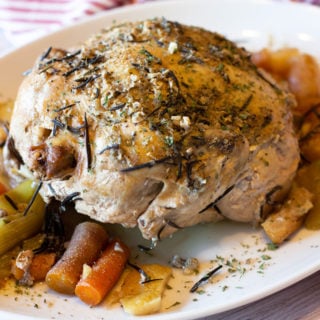 Whole chicken sitting on a platter topped with fresh rosemary.