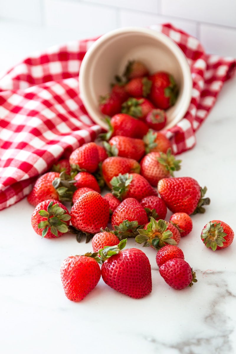 Bowl of fresh whole strawberries spread out on a counter. 