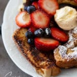 Close up of french toast topped with powdered sugar, berries, and butter.