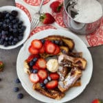 Plate containing french toast topped with strawberries, blueberries, and powdered sugar.