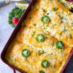Casserole dish containing chicken enchiladas topped with cheese and sliced peppers.